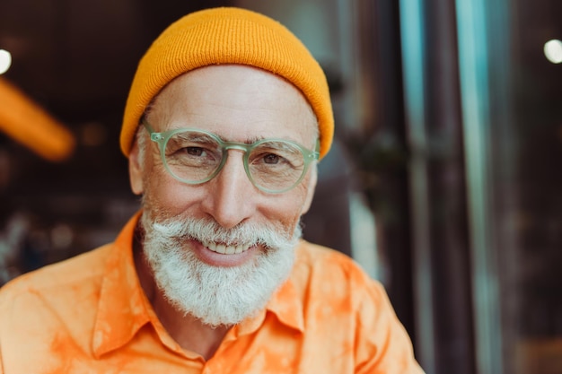 Ritratto di un uomo anziano attraente che indossa abiti casual eleganti, cappello giallo e occhiali da vista sorridente guardando la fotocamera Bel hipster maschio senior in posa per lo spazio della copia dell'immagine Concetto di visione