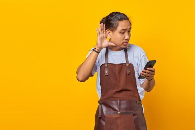 Ritratto di un uomo asiatico dall'aspetto serio che cerca di ascoltare una conversazione segreta e tiene in mano uno smartphone