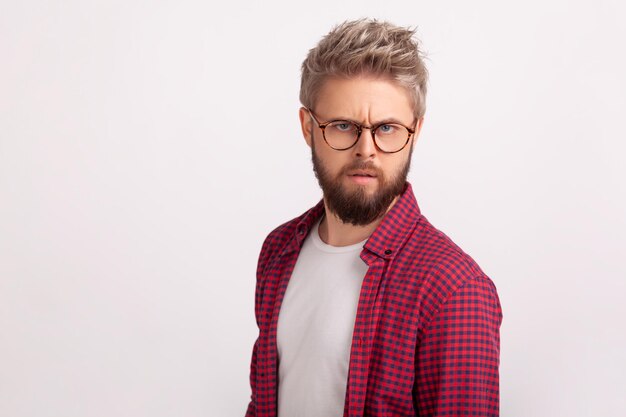 Ritratto di un uomo barbuto biondo perplesso che indossa occhiali accigliato e guarda seriamente la fotocamera Scatto in studio al coperto isolato su sfondo grigio