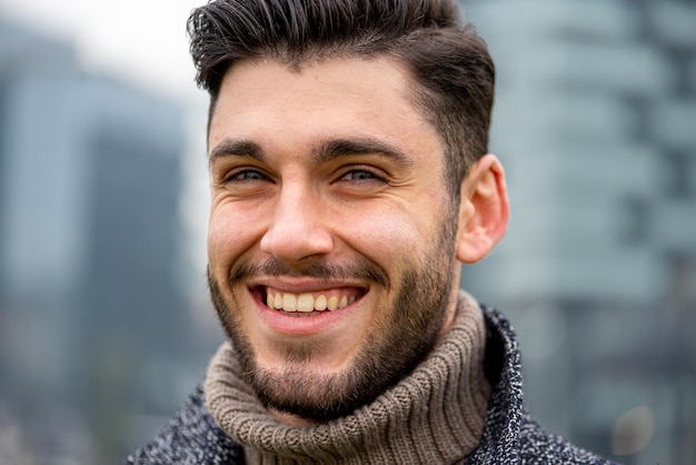 Ritratto di un uomo barbuto sorridente primo piano di un modello maschile con occhi azzurri felice espressione facciale sfondo urbano e skyline