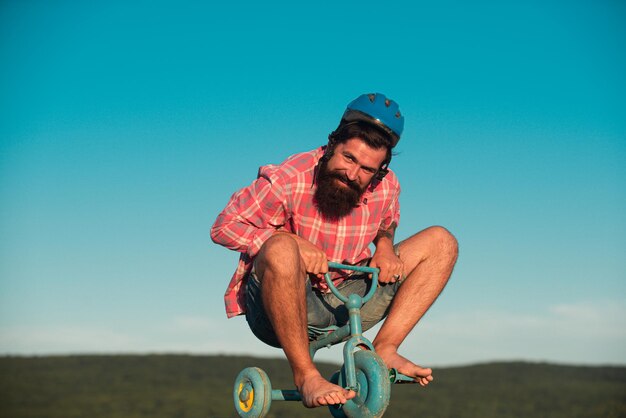 Ritratto di un uomo barbuto, un hipster pazzo che si diverte con la bicicletta all'aperto.