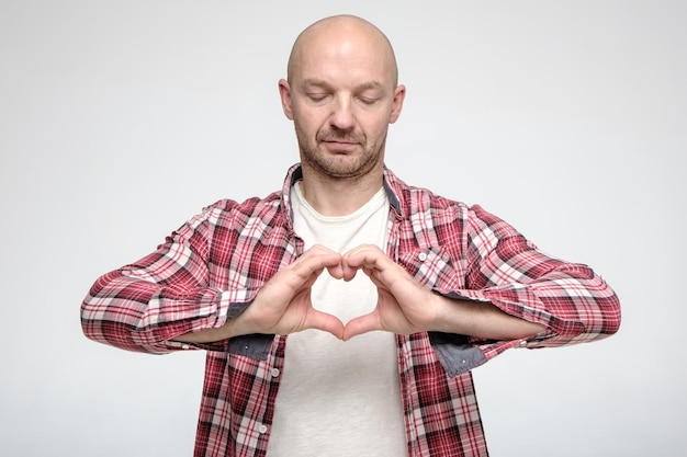 Ritratto di un uomo calvo con la barba lunga che sta cercando di fare una forma a cuore con le dita