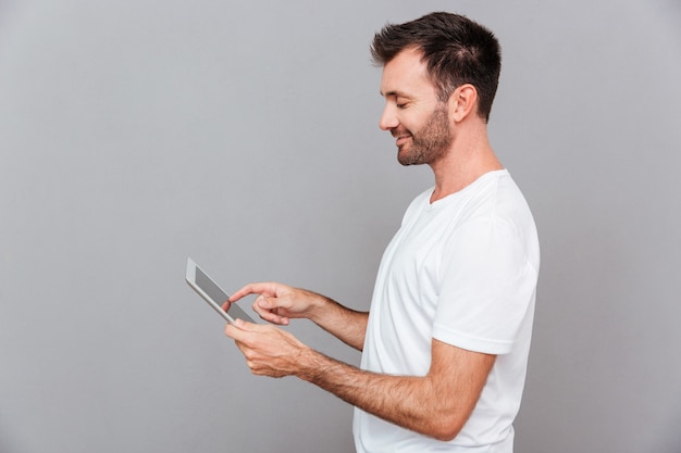 Ritratto di un uomo casual sorridente che tiene in mano un tablet su sfondo grigio