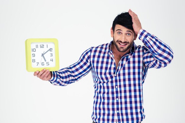 Ritratto di un uomo casual tenendo l'orologio da parete e guardando la parte anteriore isolata su un muro bianco