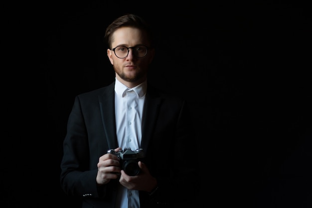 Ritratto di un uomo che indossa in abito nero elegante che guarda l'obbiettivo e che tiene macchina fotografica