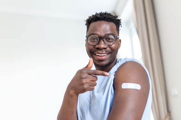 Ritratto di un uomo che sorride dopo aver ricevuto un vaccino Uomo africano che tiene giù la manica della camicia e mostra il braccio con la benda dopo aver ricevuto la vaccinazione