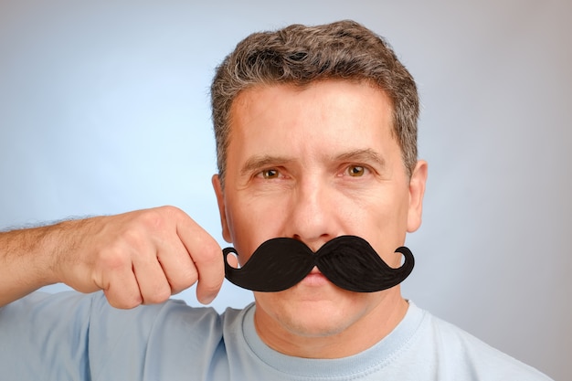 Ritratto di un uomo con i baffi finti in mano per partecipare a un evento a novembre per aiutare gli uomini a conoscere i problemi di salute.