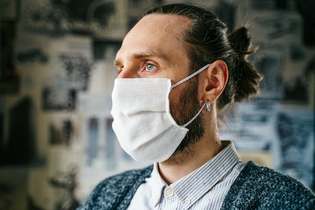 Ritratto di un uomo con la barba in una maschera di garza Ritratto di un uomo con la barba in una maschera di garza. Protezione preventiva della propria salute dalle infezioni virali. Concetto di coronavirus.