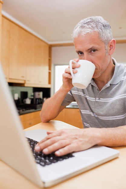 Ritratto di un uomo con un computer portatile mentre si beve il tè