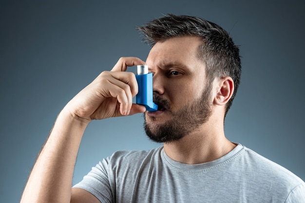Ritratto di un uomo con un inalatore per l'asma in mano, un attacco asmatico. Il concetto di trattamento di asma bronchiale, tosse, allergie, dispnea.