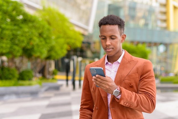 Ritratto di un uomo d'affari africano all'aperto utilizzando il telefono cellulare e indossando abiti eleganti