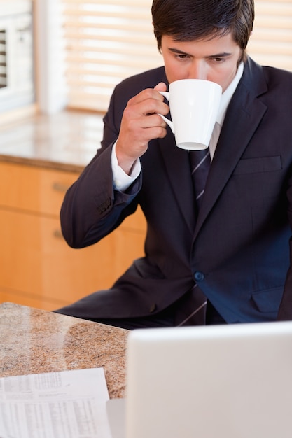 Ritratto di un uomo d&#39;affari che beve caffè durante l&#39;utilizzo di un computer portatile