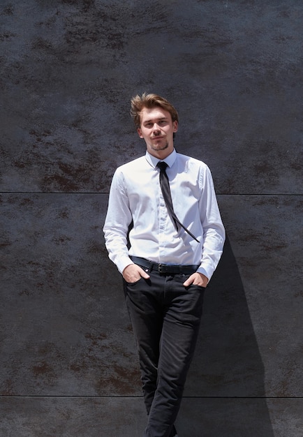ritratto di un uomo d'affari di avvio in una camicia bianca con una cravatta nera in piedi davanti al muro grigio all'esterno