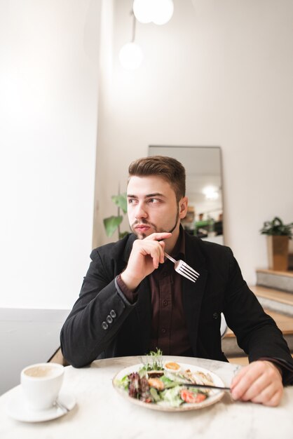 Ritratto di un uomo d'affari di mangiare un'insalata appetitosa in un accogliente ristorante leggero e guardando la finestra