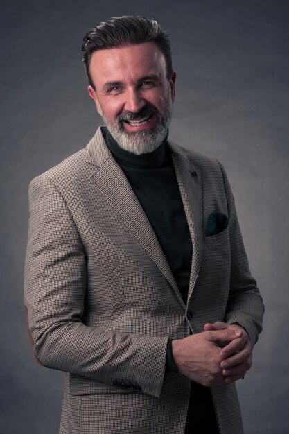 Ritratto di un uomo d'affari senior elegante ed elegante con la barba e abiti da lavoro casual in studio fotografico isolato su sfondo scuro che gesturing con le mani. Foto di alta qualità