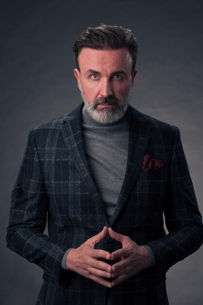 Ritratto di un uomo d'affari senior elegante ed elegante con la barba e abiti da lavoro casual in studio fotografico isolato su sfondo scuro che gesturing con le mani. Foto di alta qualità