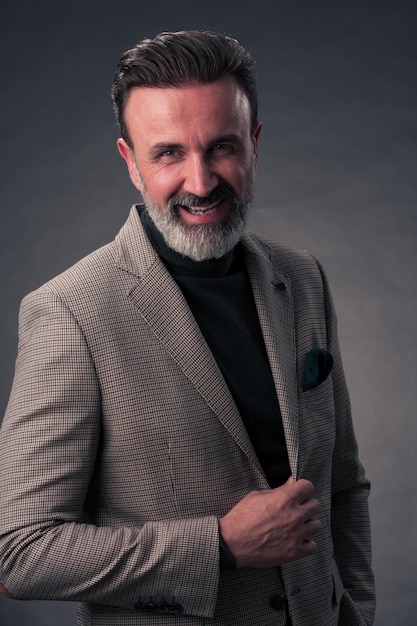 Ritratto di un uomo d'affari senior elegante ed elegante con la barba e abiti da lavoro casual in studio fotografico isolato su sfondo scuro che gesturing con le mani. Foto di alta qualità