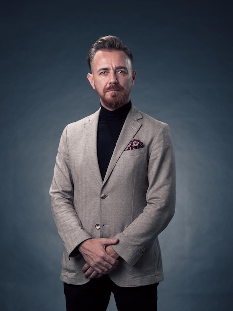 Ritratto di un uomo d'affari senior elegante ed elegante di successo con una barba grigia e abiti casual da lavoro fiducioso nello studio fotografico isolato su sfondo scuro che gesticola con le mani. Foto di alta qualità