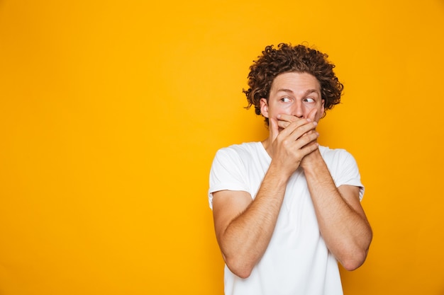 Ritratto di un uomo dai capelli ricci scioccato che copre la bocca