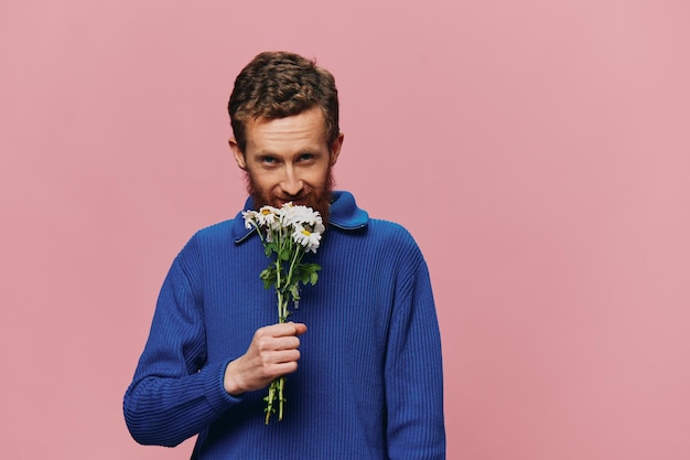 Ritratto di un uomo divertente sorridente con un mazzo di fiori margherite su sfondo rosa isolato copia posto Concetto di vacanza e congratulazioni San Valentino Festa della donna