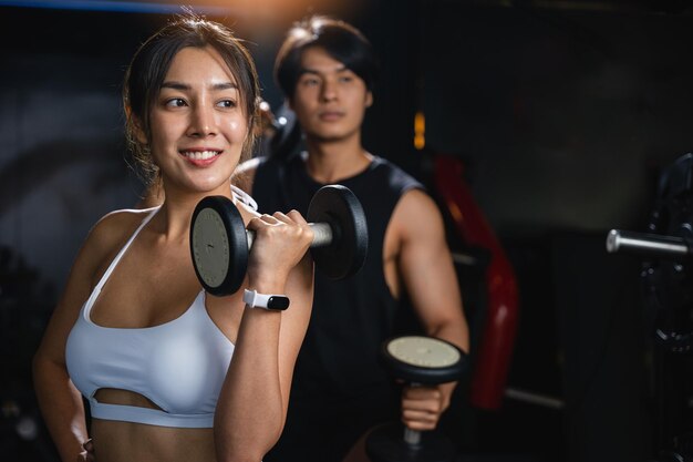 Ritratto di un uomo e una donna asiatici forti e atletici che si allenano in una palestra con barbellini