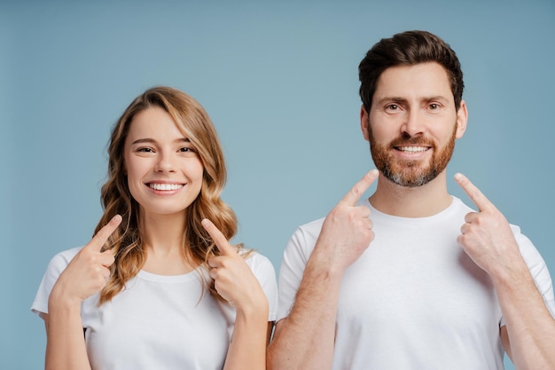 Ritratto di un uomo e una donna attraenti che sorridono e puntano le dita sui denti indossando magliette bianche