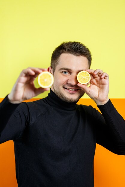 Ritratto di un uomo elegante in raglan nero con un limone a fette nelle sue mani. Ragazzo alla moda. Un sorriso sul suo volto