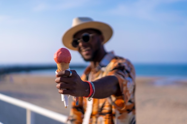 Ritratto di un uomo etnico nero godersi le vacanze estive in spiaggia a mangiare il gelato
