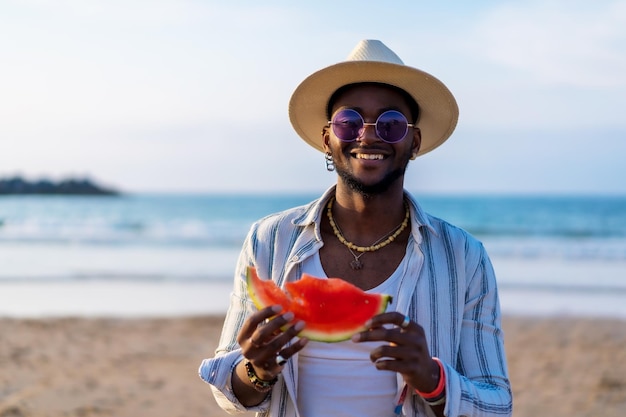 Ritratto di un uomo etnico nero godersi le vacanze estive sulla spiaggia mangiando un'anguria in riva al mare