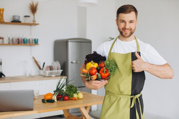 Ritratto di un uomo felice che tiene un piatto di verdure fresche sullo sfondo della cucina di casa