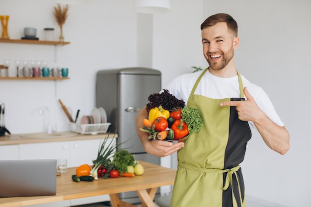 Ritratto di un uomo felice che tiene un piatto di verdure fresche sullo sfondo della cucina di casa