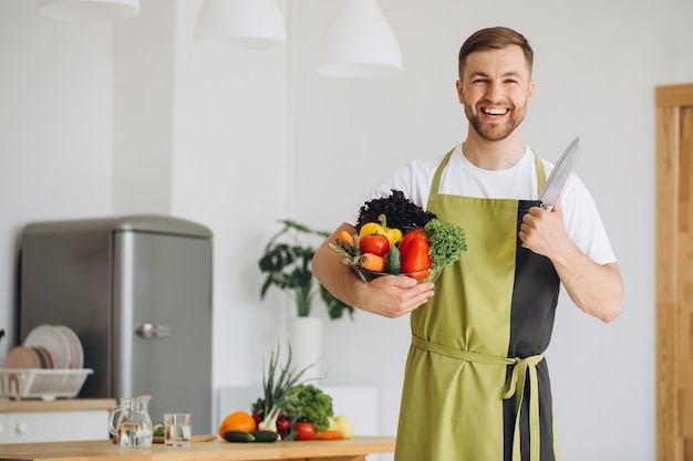 Ritratto di un uomo felice che tiene un piatto di verdure fresche sullo sfondo della cucina di casa