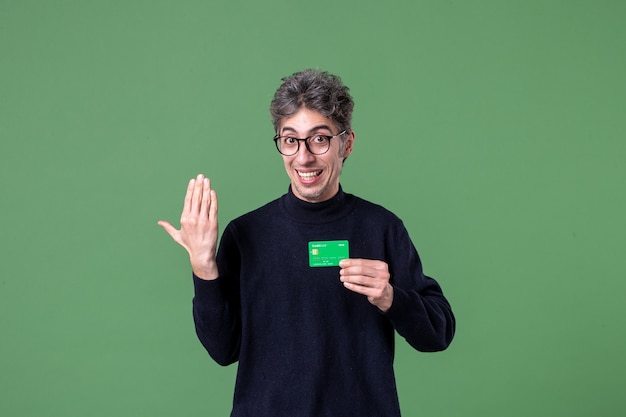 Ritratto di un uomo geniale che tiene in mano una carta di credito verde sulla parete verde