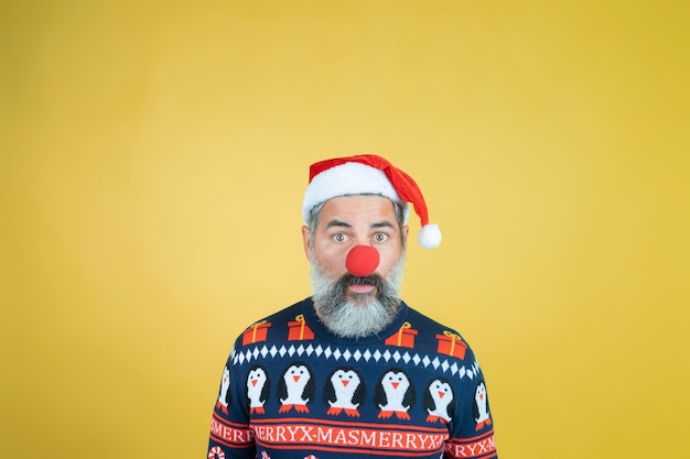 Ritratto di un uomo in cappello di Babbo Natale con naso rosso da clown su giallo