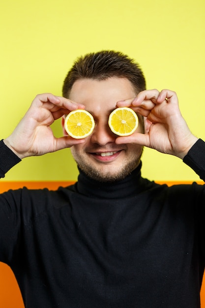 Ritratto di un uomo in raglan nero con limone tagliato al posto degli occhi. Un tipo con dei limoni vicino al viso. Un sorriso sul suo volto