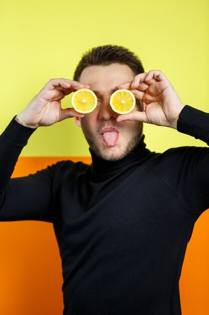 Ritratto di un uomo in raglan nero con limone tagliato al posto degli occhi. Un tipo con dei limoni vicino al viso. Un sorriso sul suo volto