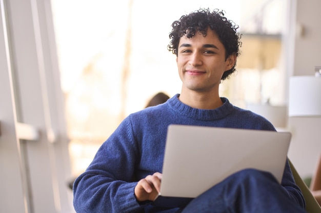 Ritratto di un uomo latinoamericano positivo sorridente bello con il computer portatile che guarda con confidenza la macchina fotografica