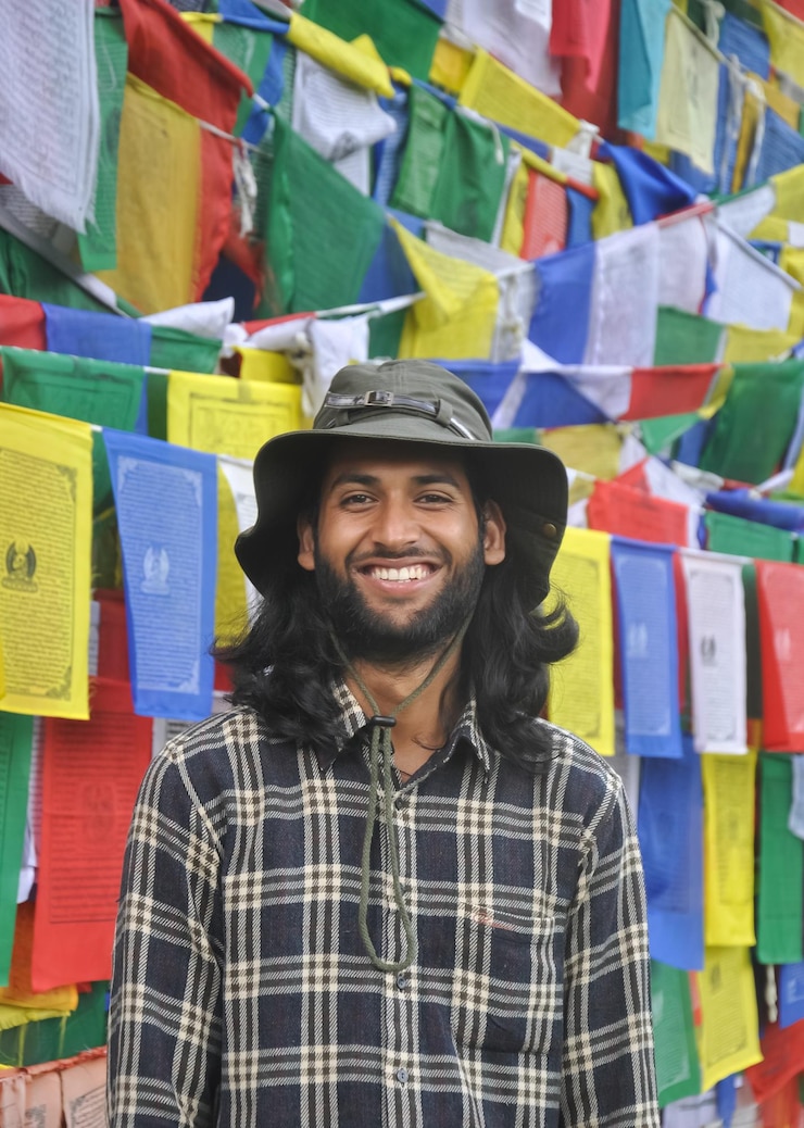 Foto ritratto di un uomo sorridente che indossa un cappello contro le bandiere di preghiera