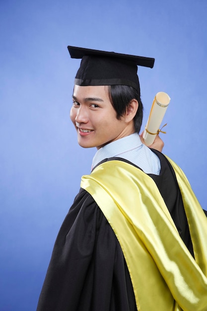 Ritratto di un uomo sorridente in abito da laurea con un certificato su sfondo blu