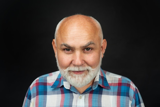 Ritratto di un vecchio uomo maturo calvo con la barba grigia sullo sfondo di uno studio nero più vecchio