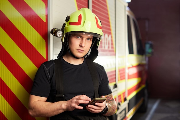 Ritratto di un vigile del fuoco in piedi davanti a un camion dei pompieri Vigile del fuoco che utilizza lo smartphone