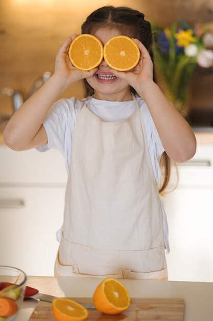 Ritratto di una bambina adorabile in grembiule in cucina e un bambino sorridente che tiene metà di