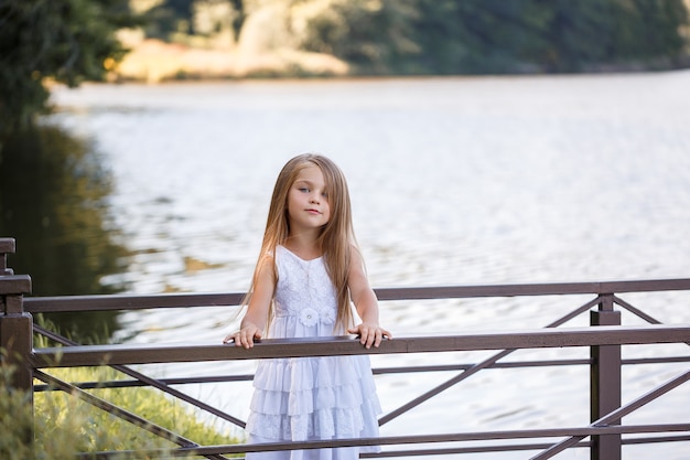 Ritratto di una bambina all'aperto in estate in riva al lago. Bambina in abito estivo in riva al fiume.