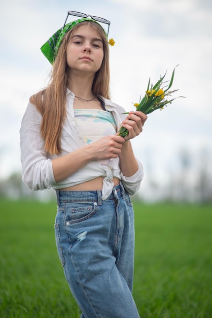 Ritratto di una bambina alla moda con un mazzo di fiori di campo in un campo verde su uno sfondo di un cielo nuvoloso