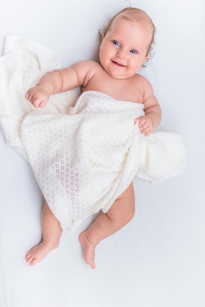 Ritratto di una bambina allegra che giace su un lenzuolo bianco ed è coperta da un panno di lana