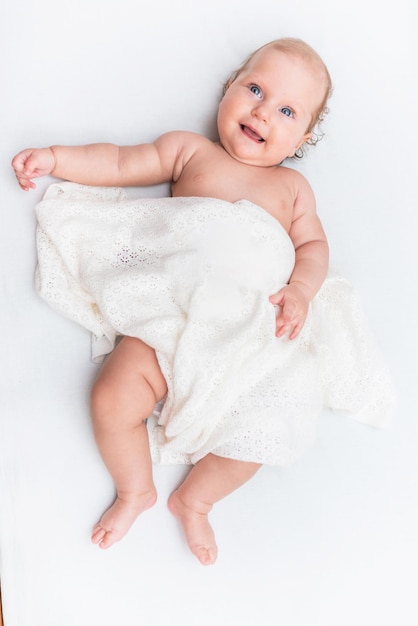 Ritratto di una bambina allegra che giace su un lenzuolo bianco ed è coperta da un panno di lana