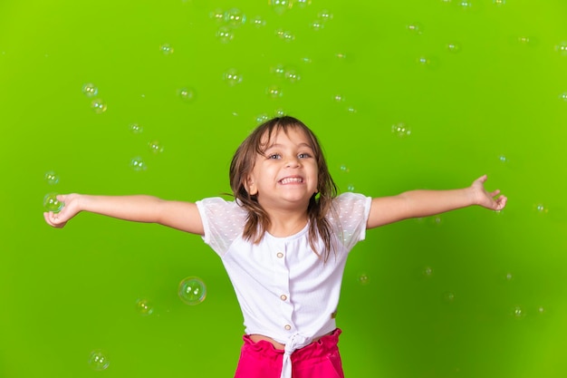 Ritratto di una bambina allegra isolata su sfondo verde che soffia bolle di sapone divertendosi