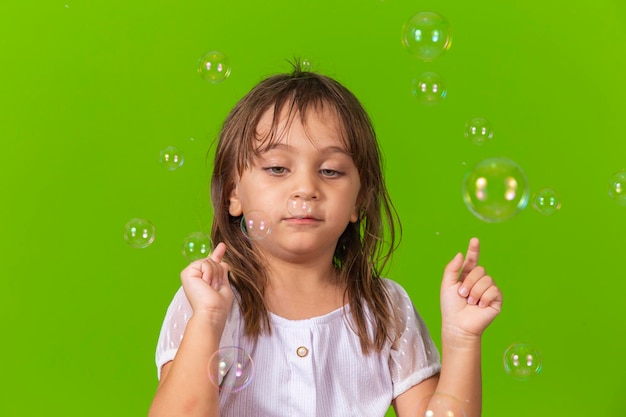 Ritratto di una bambina allegra isolata su sfondo verde che soffia bolle di sapone divertendosi