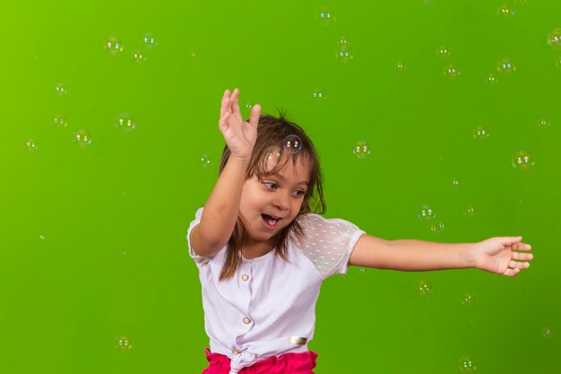 Ritratto di una bambina allegra isolata su sfondo verde che soffia bolle di sapone divertendosi