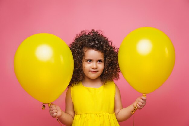 Ritratto di una bambina allegra isolata su uno sfondo rosa che tiene un mucchio di palloncini colorati in posa